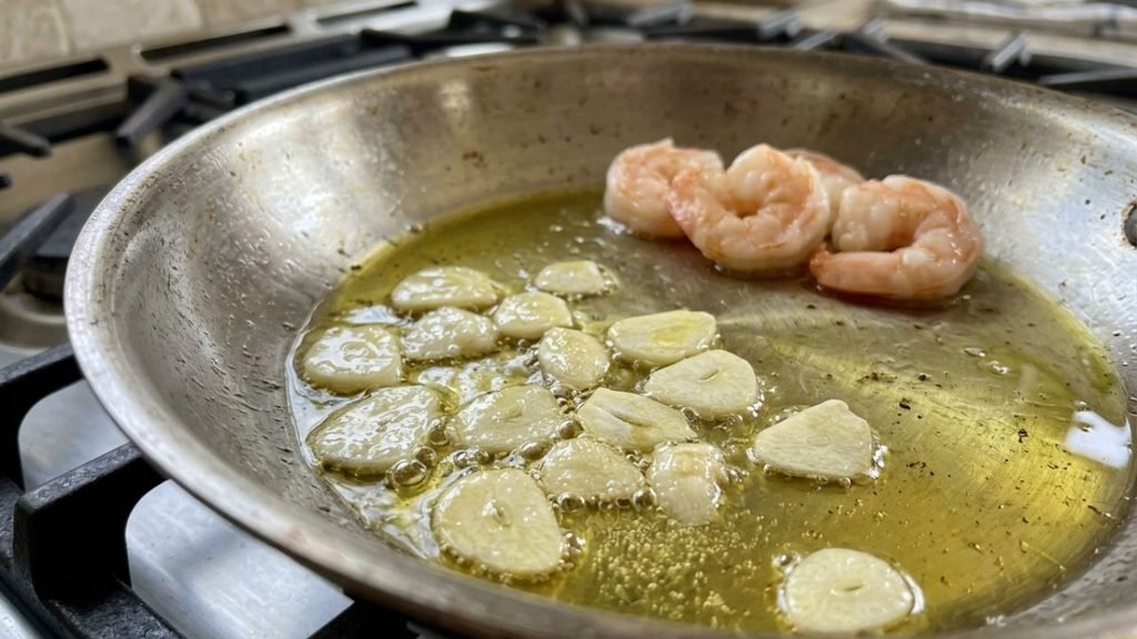 Thin garlic slices softening in olive oil in a skillet with chili flakes.