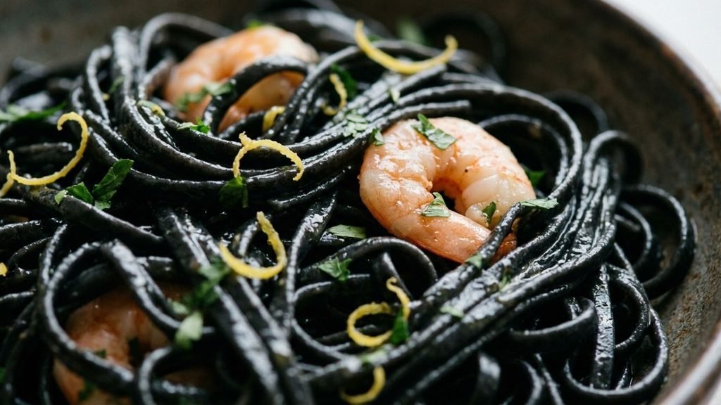 Glossy black squid ink linguine coated in sauce with pink shrimp, parsley and lemon zest.